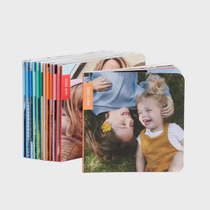 Photo books stand upright, featuring smiling children lying on grass. The front cover displays 