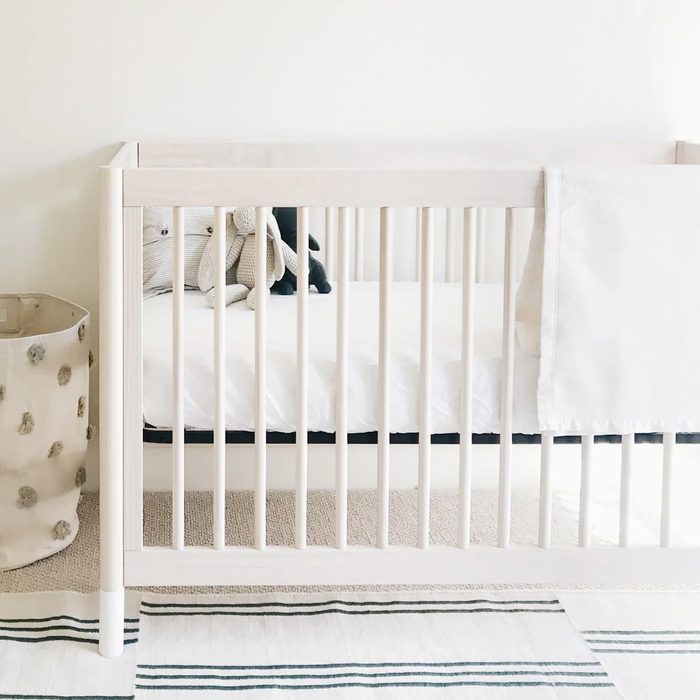 Crib holding stuffed animals in a minimalist nursery with a striped rug and soft lighting.