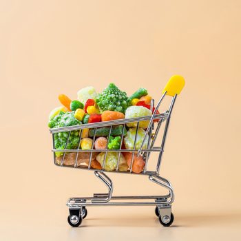 Shopping cart holds frozen vegetables against a plain, light peach background.