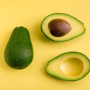 Whole avocado and two halves rest on a bright yellow surface.