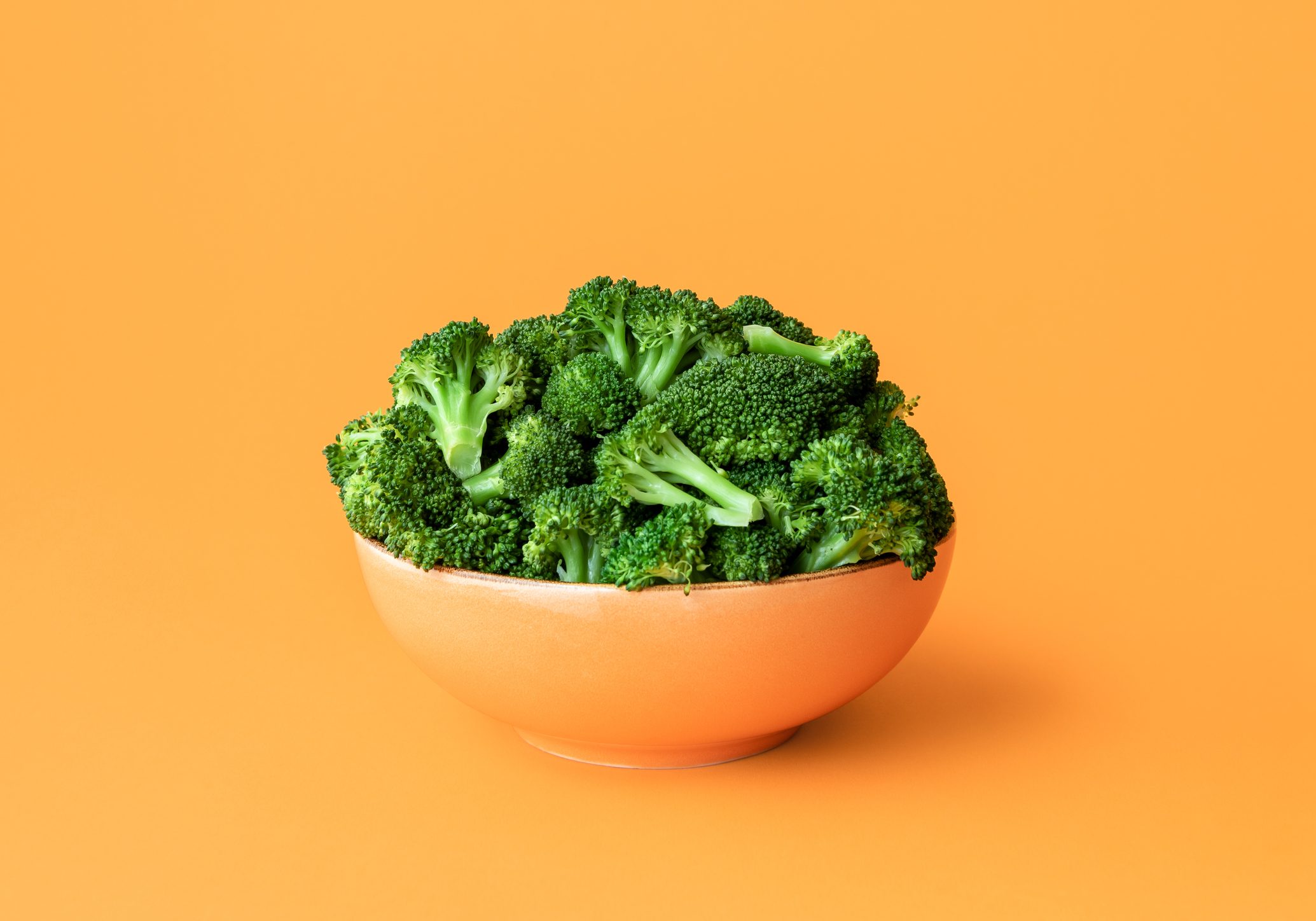 Cooked broccoli in a bowl isolated on an orange background.