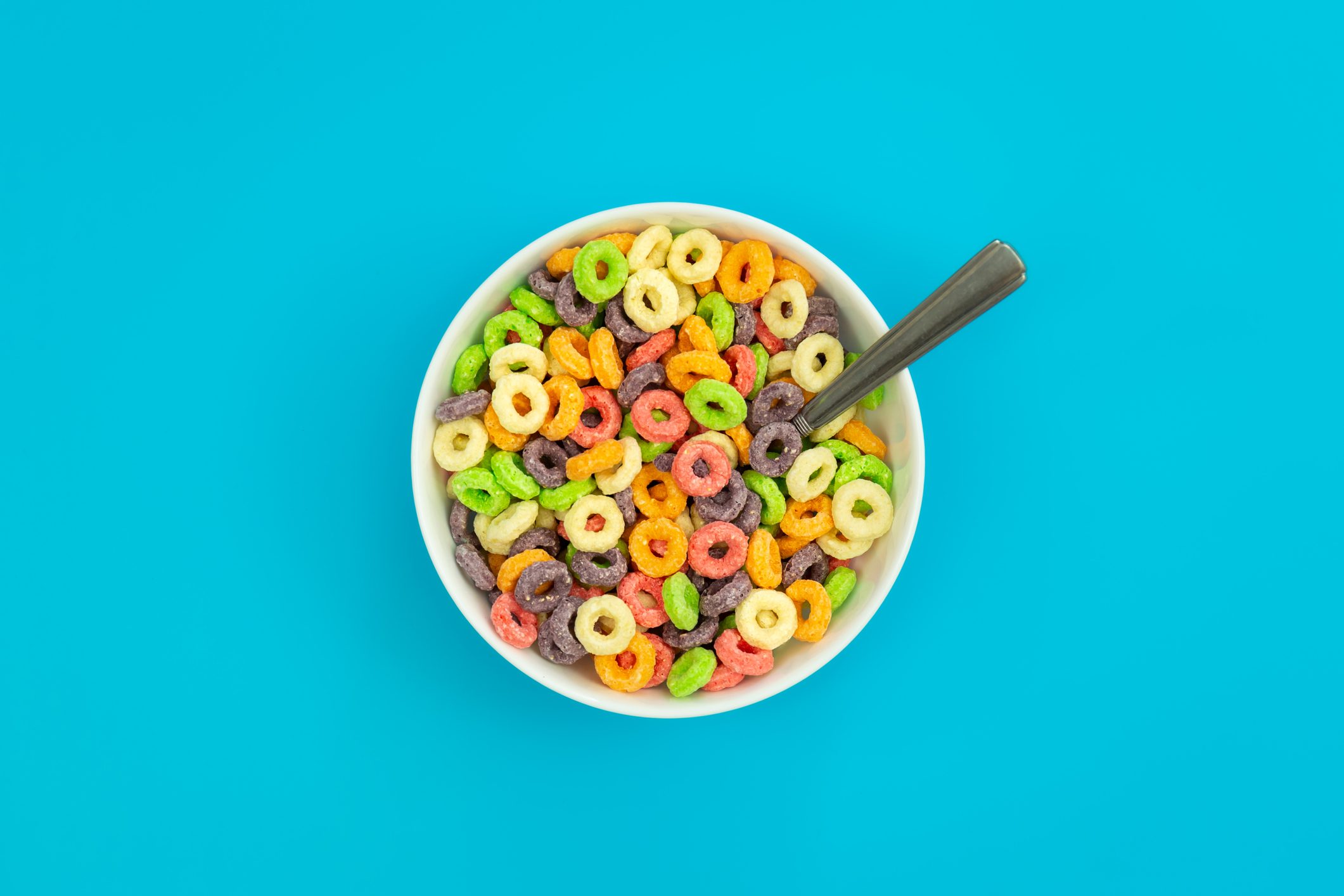 A bowl of colorful cereal with a spoon, resting on a bright blue background.