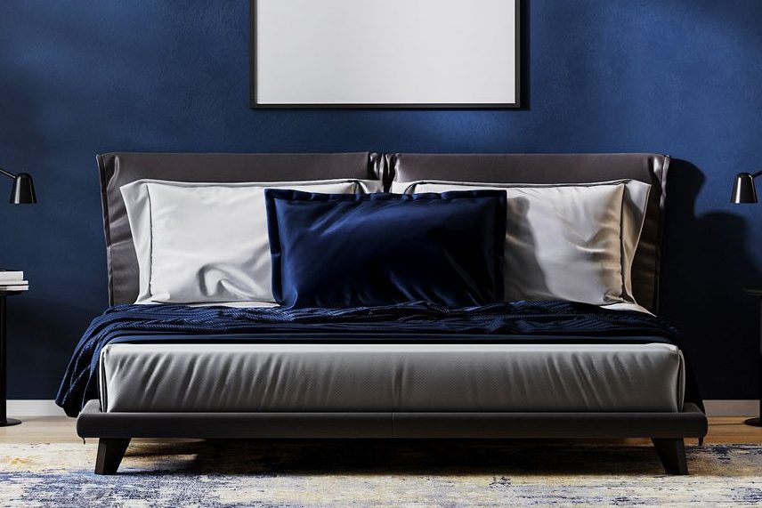 Bed with white and blue bedding placed against a navy wall, flanked by black lamps on side tables.