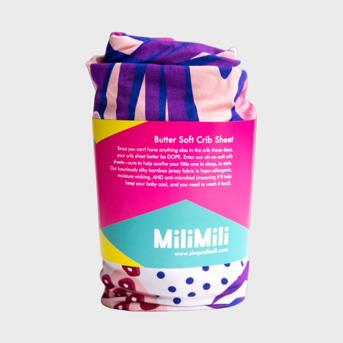 Crib sheet packaged with vibrant fabric and colorful wrapper, displaying text about softness, hypoallergenic features, and branding as 