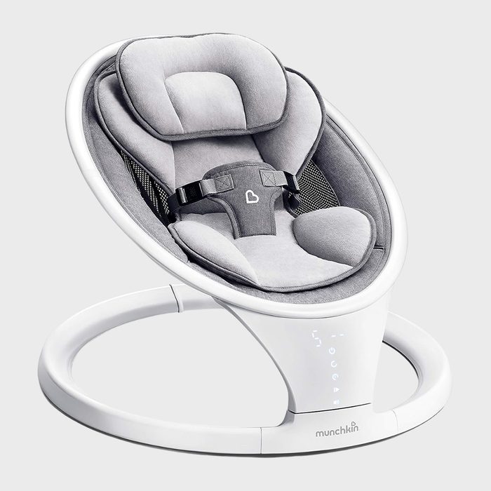 Baby rocker sits stationary, featuring a padded grey seat with safety harness, in a white plastic frame. Text: 