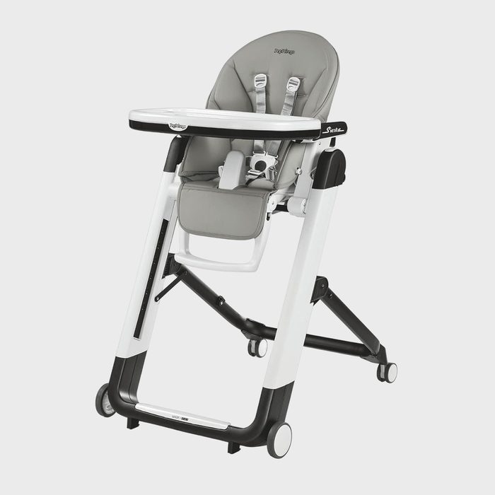 High chair stands with tray attached, featuring gray padding and safety harness; located in a plain, light-colored environment. 