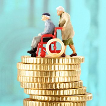 Miniature elderly couple pushes wheelchair atop stacked coins, set against a blue background.