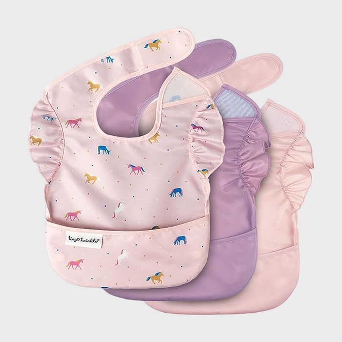 Bib features unicorns, lying flat; pastel colors, ruffled sides, Velcro neck. Other bibs in lavender and pink appear stacked beneath. Text reads 