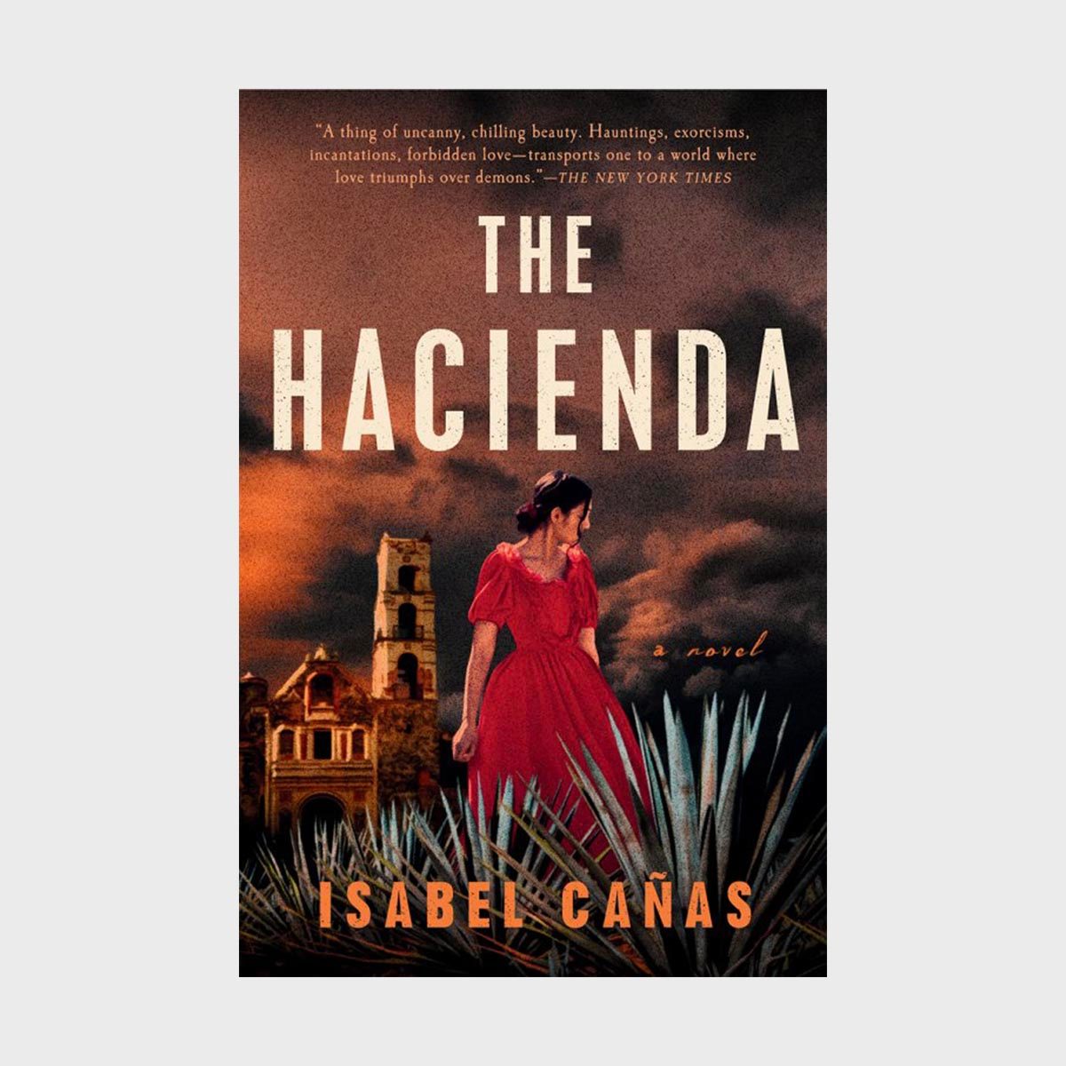 Woman in red dress stands looking aside, surrounded by agave plants, set against a dramatic sky and old building. Text: "The Hacienda," "Isabel Ca&Atilde;&plusmn;as."