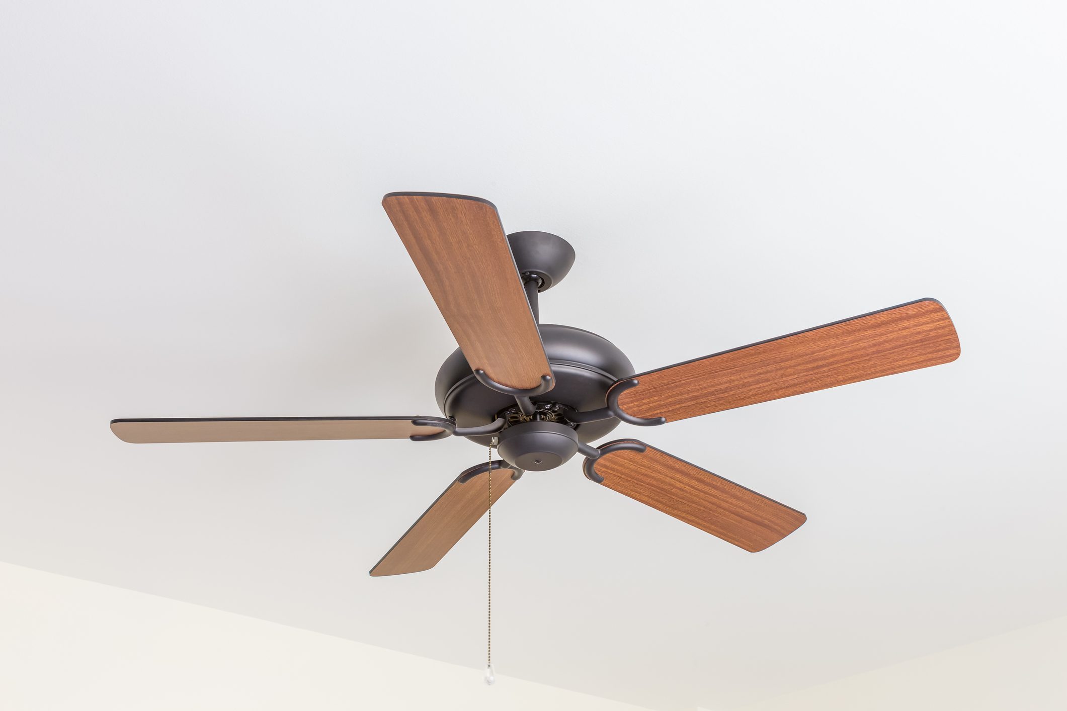 Ceiling fan with wooden blades hangs from white ceiling, chain pull slightly visible.