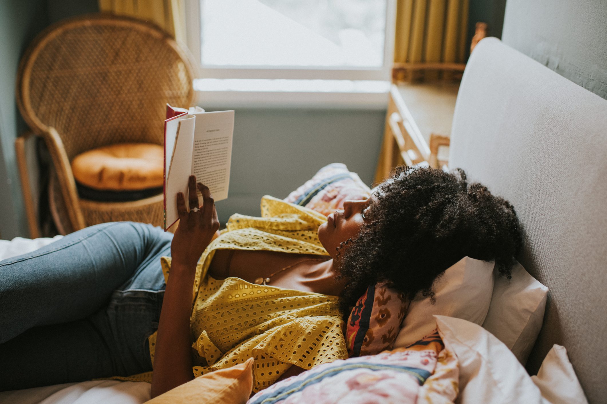 A content woman reclines on a comfortable bed and gets lost in a good book