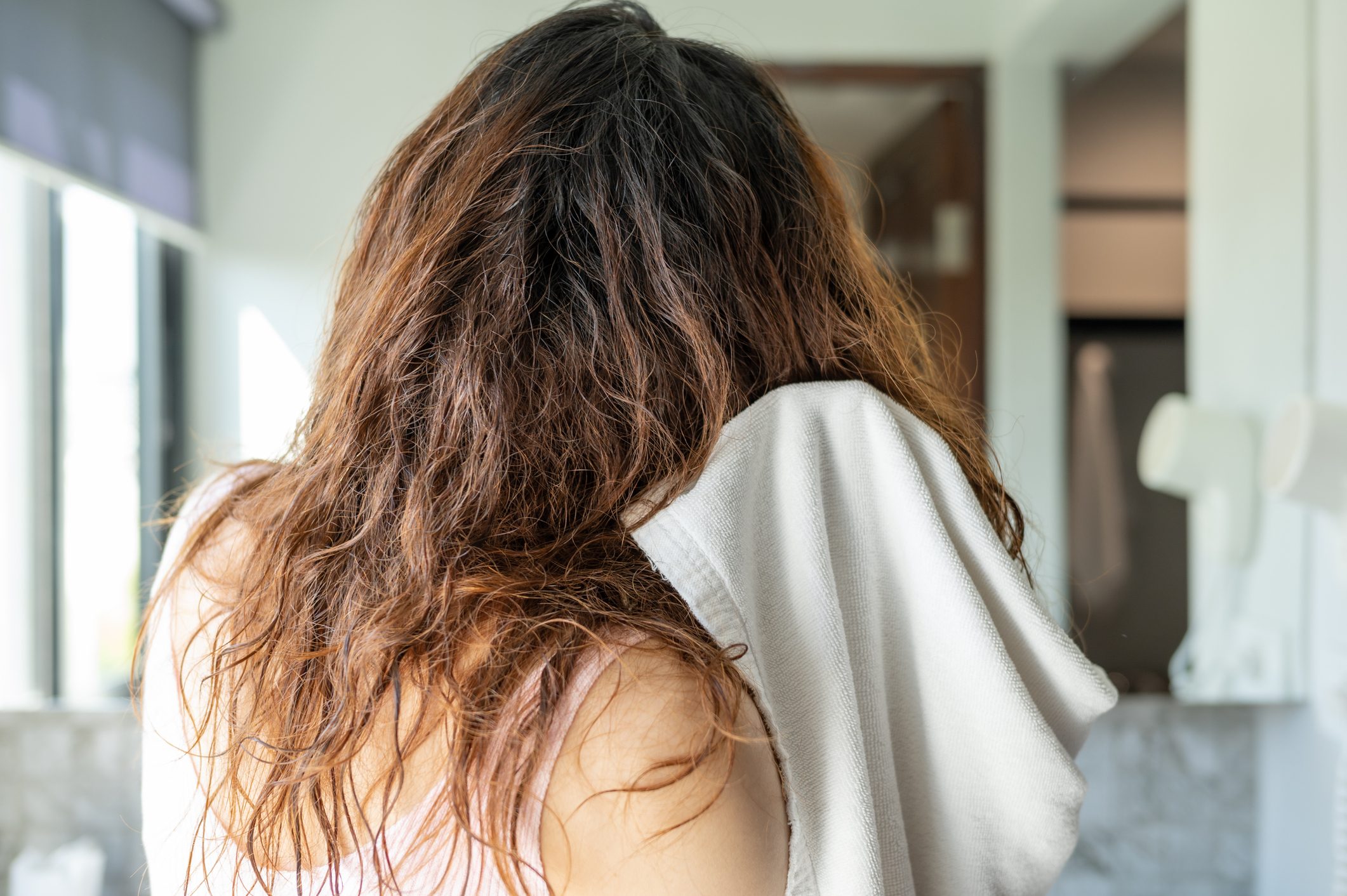 Rear view of woman dries her wet hair after shower.