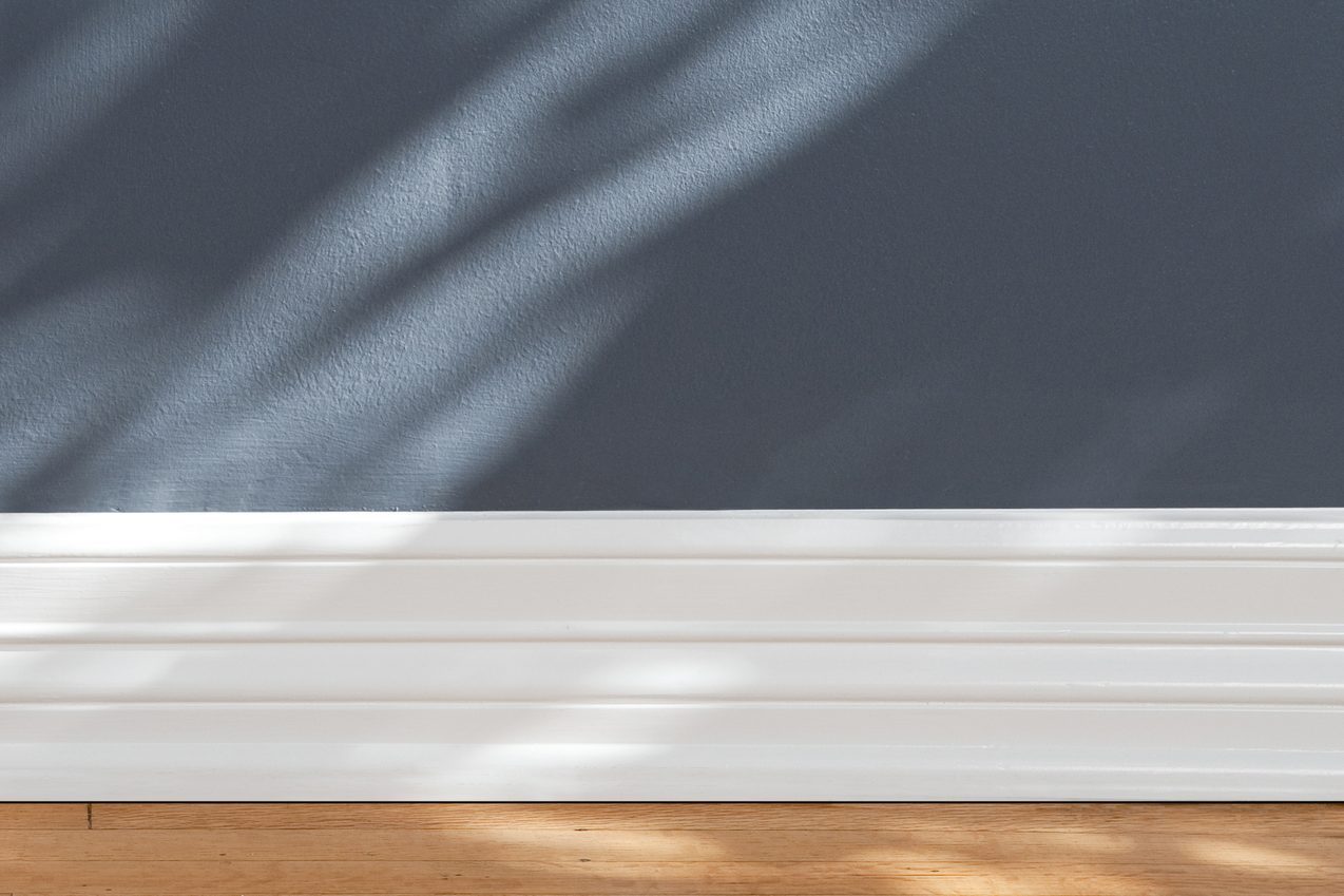 White baseboard rests against a gray wall, with sunlight casting gentle shadows, above a wooden floor.