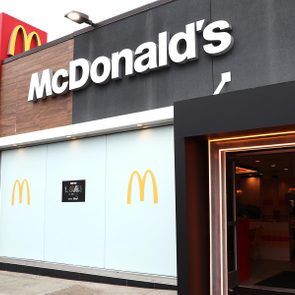 McDonald's entrance, illuminated, in urban setting with promotional posters and iconic golden arches on walls.