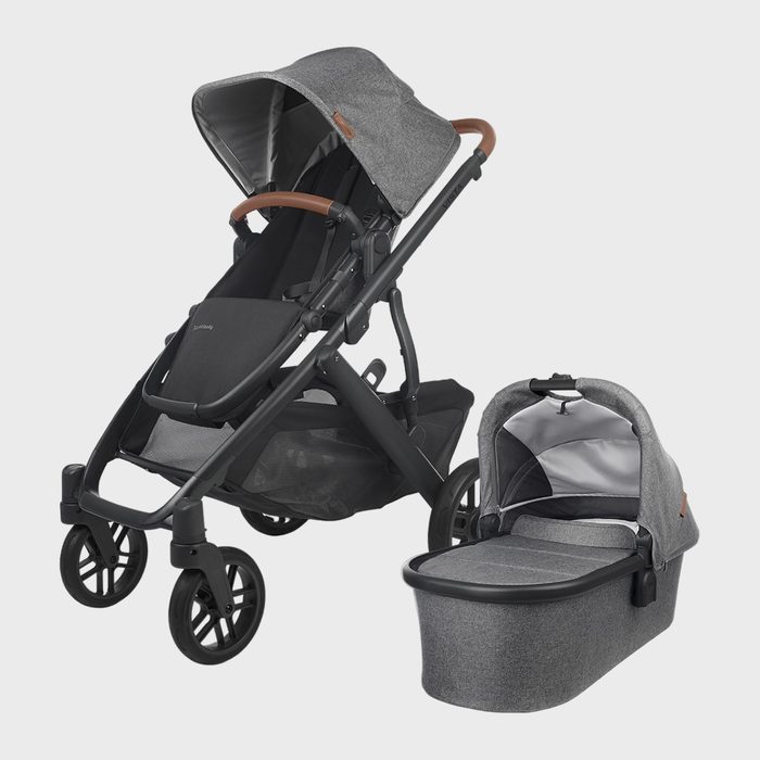 Stroller and bassinet set placed on a plain background, featuring a gray fabric design with a brown handle and four black wheels.