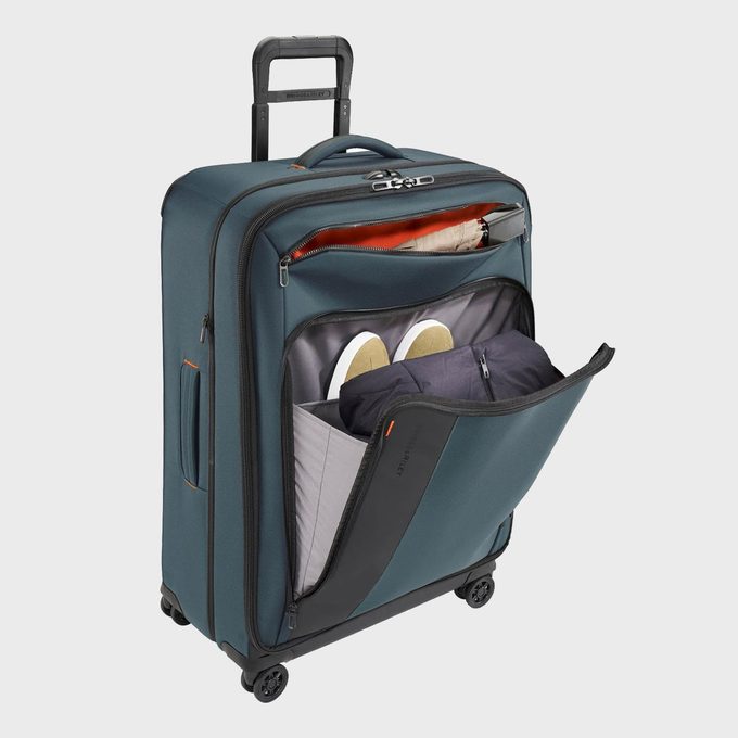 Suitcase stands upright, displaying an open zippered compartment containing clothes and shoes. It's situated against a plain background, featuring extended handles.
