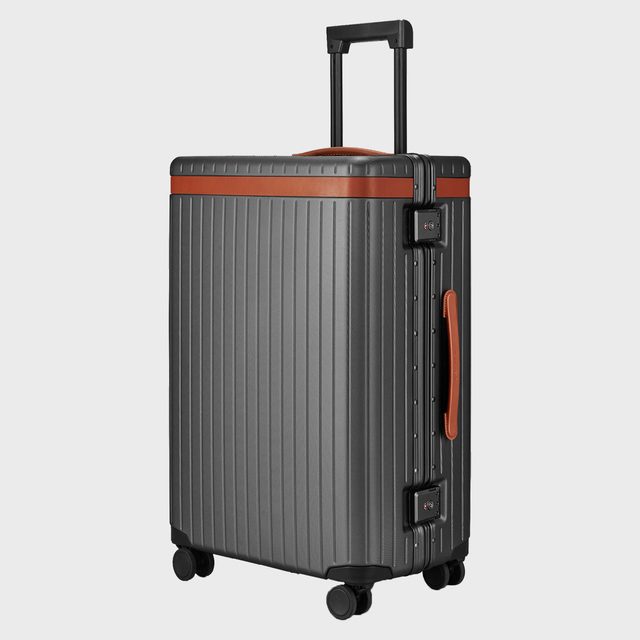 Suitcase stands upright, featuring ribbed texture and four wheels, surrounded by a plain light gray background.