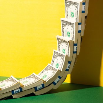 Stacks of dollar bills curve against a yellow backdrop, highlighted by green flooring and blue bands marked "$100."