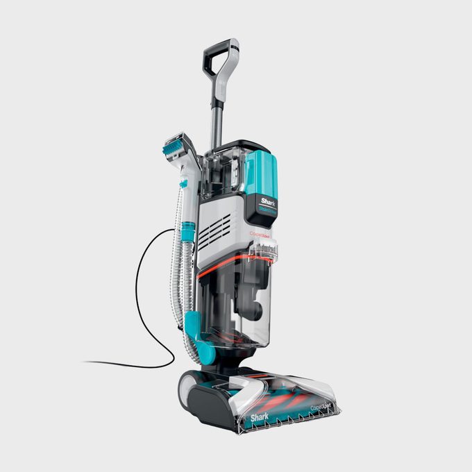 Vacuum cleaner standing upright, equipped with a transparent container and a hose attachment, set against a plain gray background.