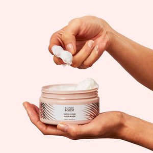 Hand scoops cream from Bondi Boost Rapid Repair Hair Mask jar in a minimalist setting.
