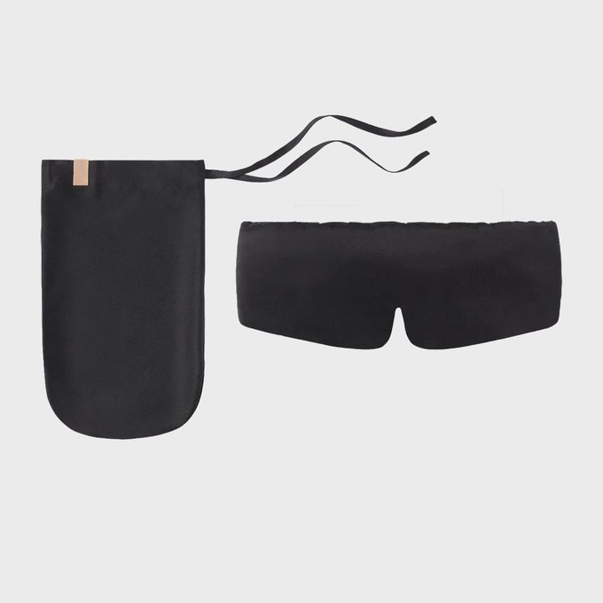 A black sleep mask with straps lies next to a matching pouch, against a plain white background.