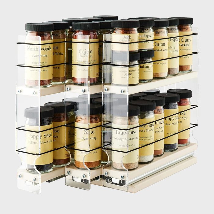 Spice rack holding various labeled seasoning jars; arranged neatly in a transparent, multi-tiered organizer against a plain background.