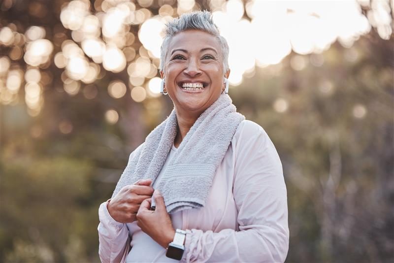 Person smiling, holding a towel over shoulders, standing outdoors with trees in the background.