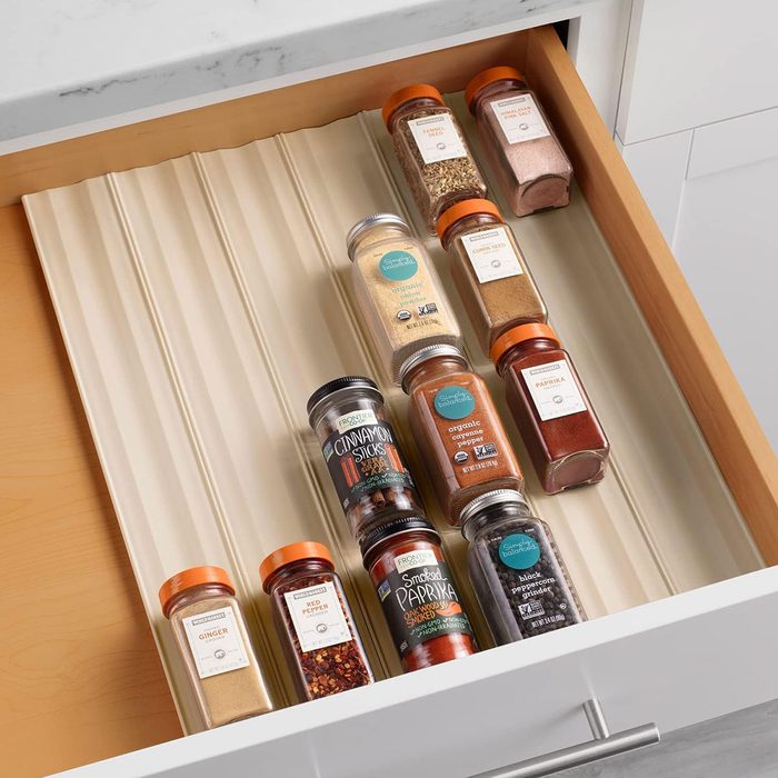 Spice jars lie organized on a ribbed tray inside a wooden kitchen drawer, under a marble countertop.