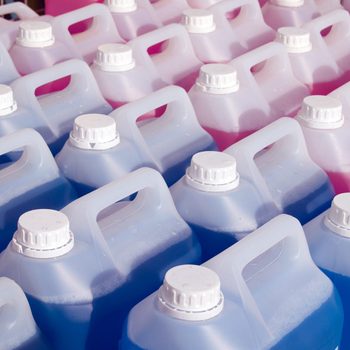 Plastic jugs are lined up, filled with blue and pink liquids, organized in multiple rows on a display.