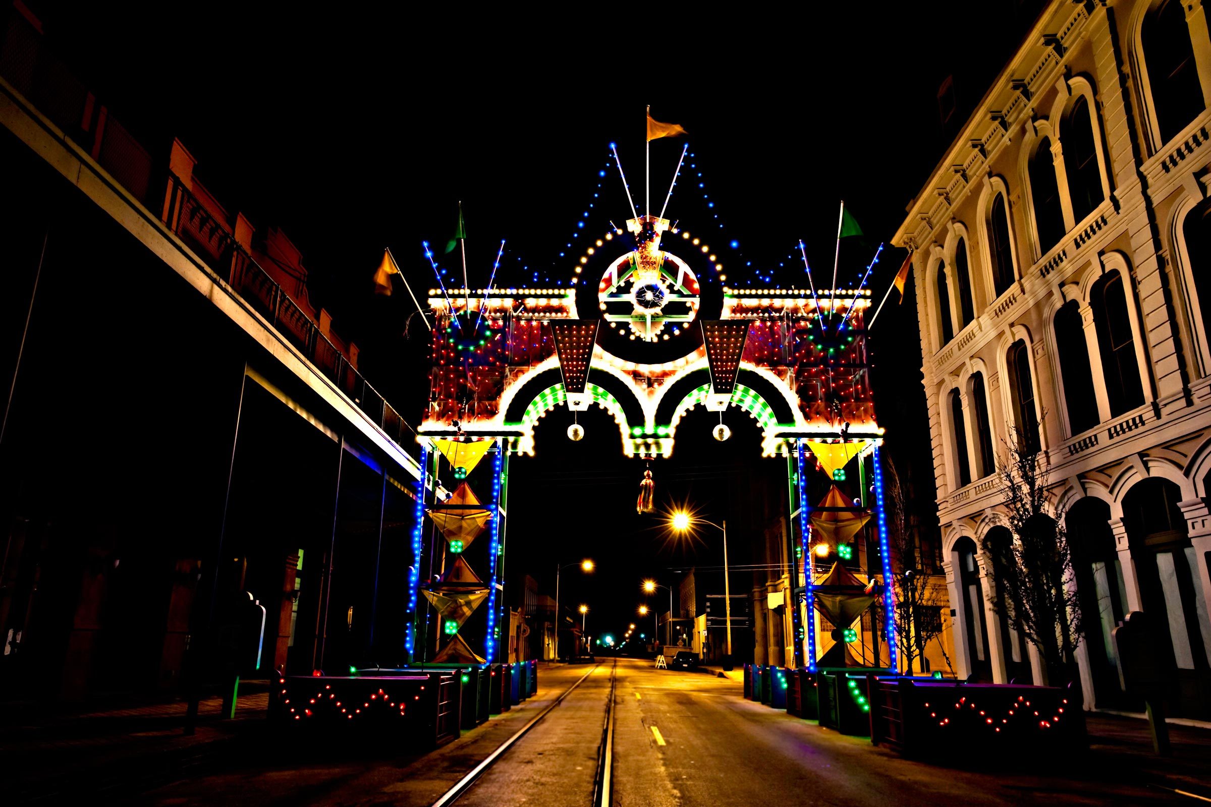 Illuminated archway displays vibrant lights, creating a festive atmosphere on a quiet street lined by historic buildings at night.