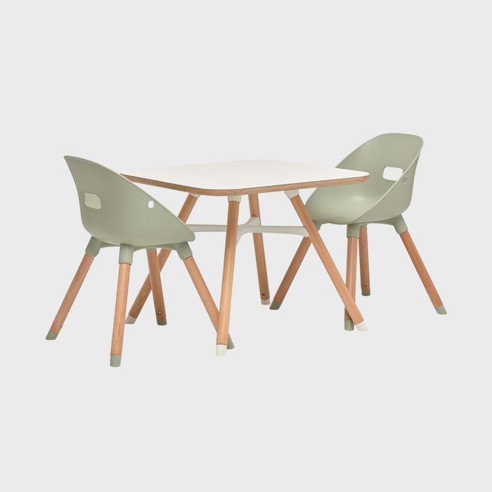 Two light green chairs with wooden legs are positioned around a small, square white table, set in a minimalist, undefined space.