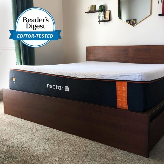 Mattress rests on wooden bed frame in a carpeted room; 