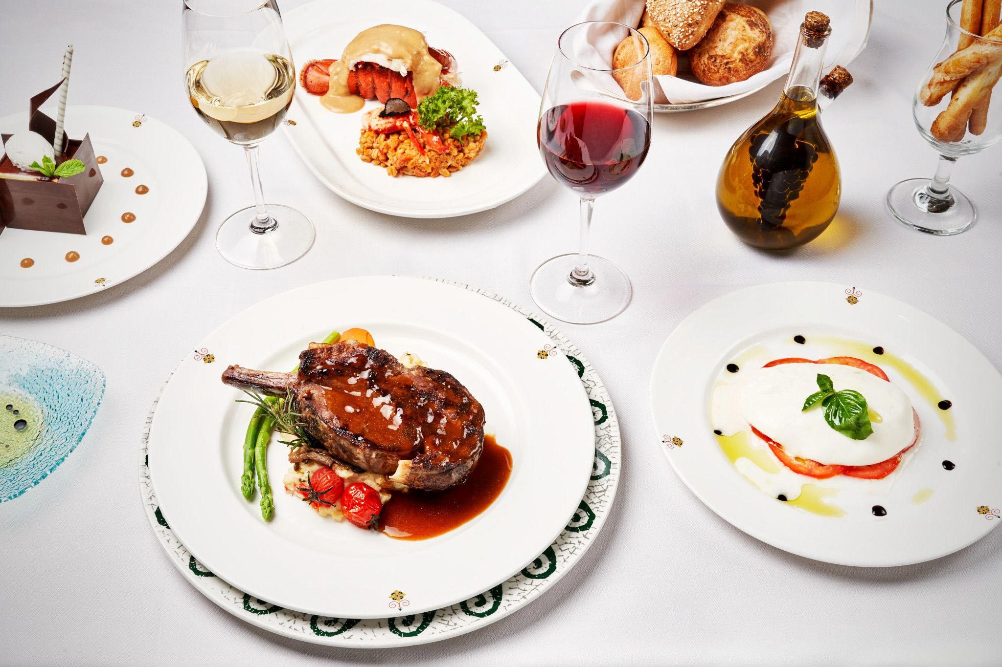 A gourmet meal, attractively plated, accompanied by wine glasses and a basket of breads on a white tablecloth.