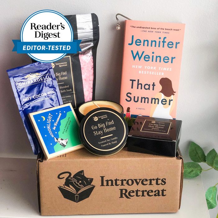 Gift box containing bath soak, candle, book, and chocolate arranged on a table; labeled 