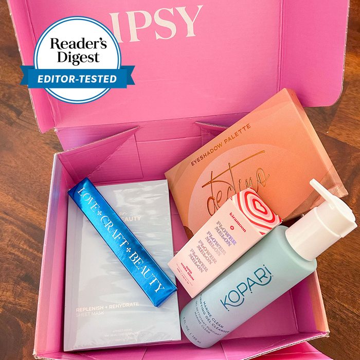 Beauty products arranged in a pink IPSY box, featuring skincare and makeup items, on a wooden surface.