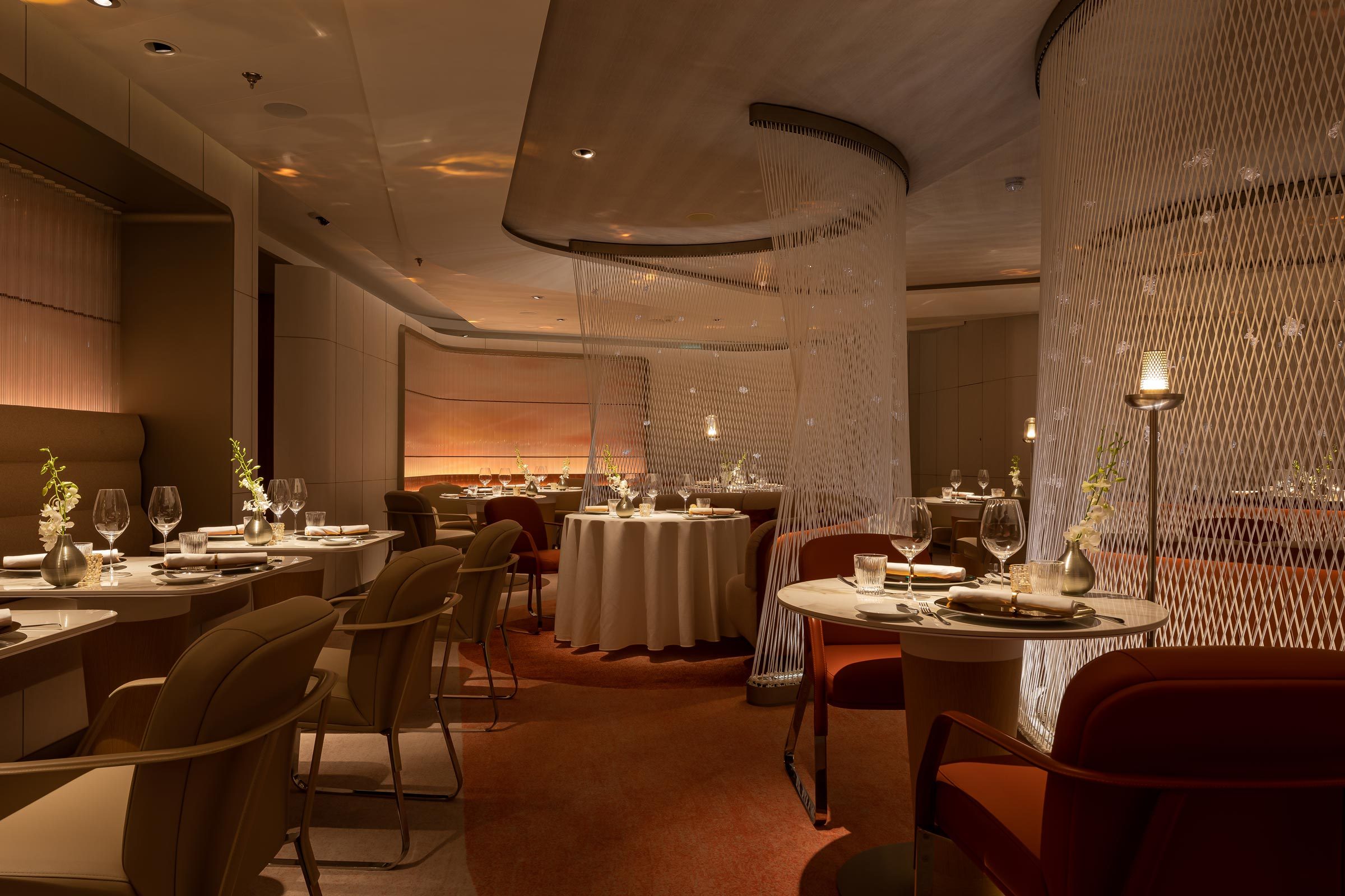 Tables set for dining, adorned with glassware and flowers, in an elegantly dim-lit restaurant with partitioned seating and modern decor.