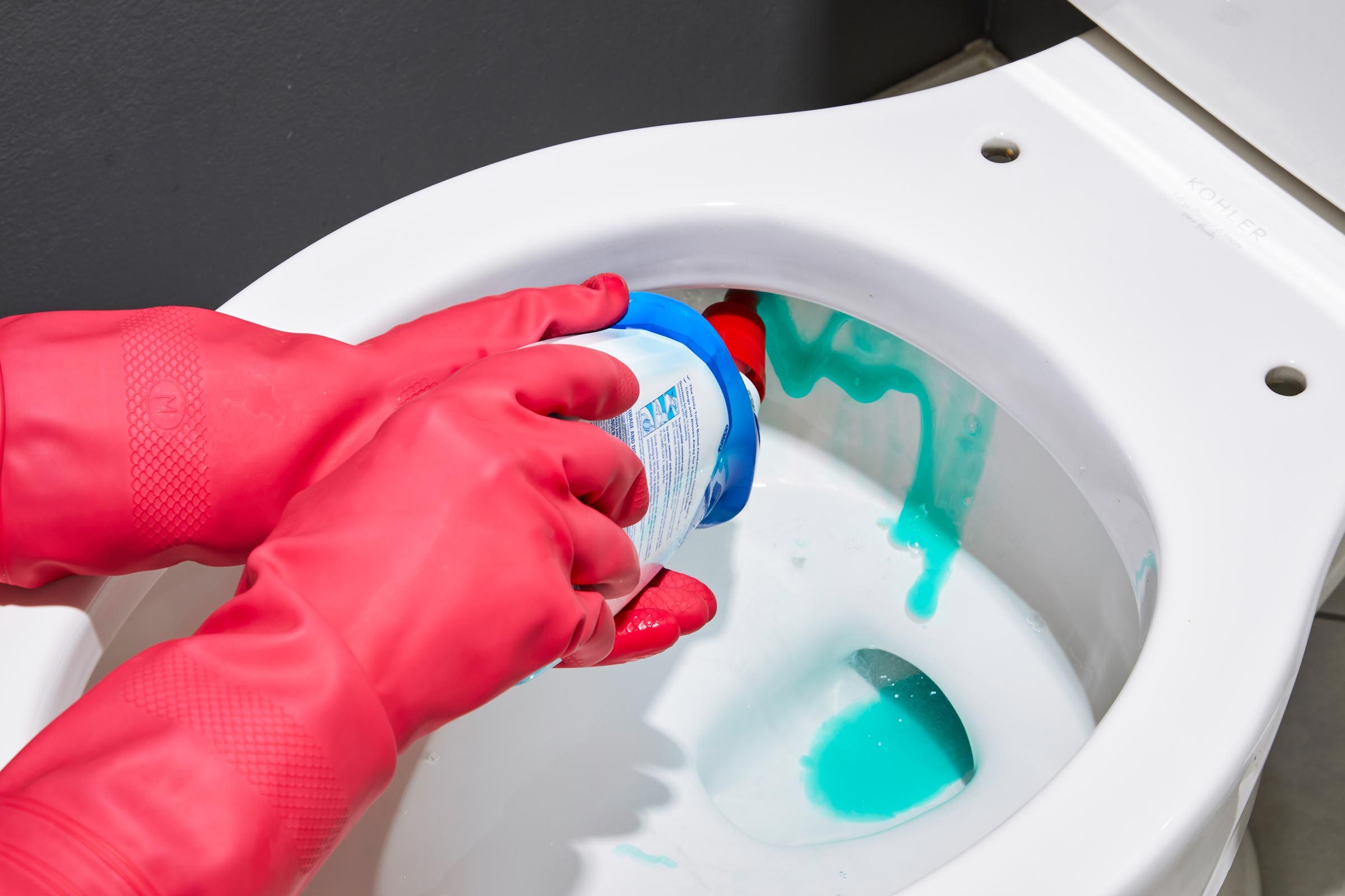 gloved hands putting lysol toilet bowl cleaner in a toilet to get rid of hard water stains