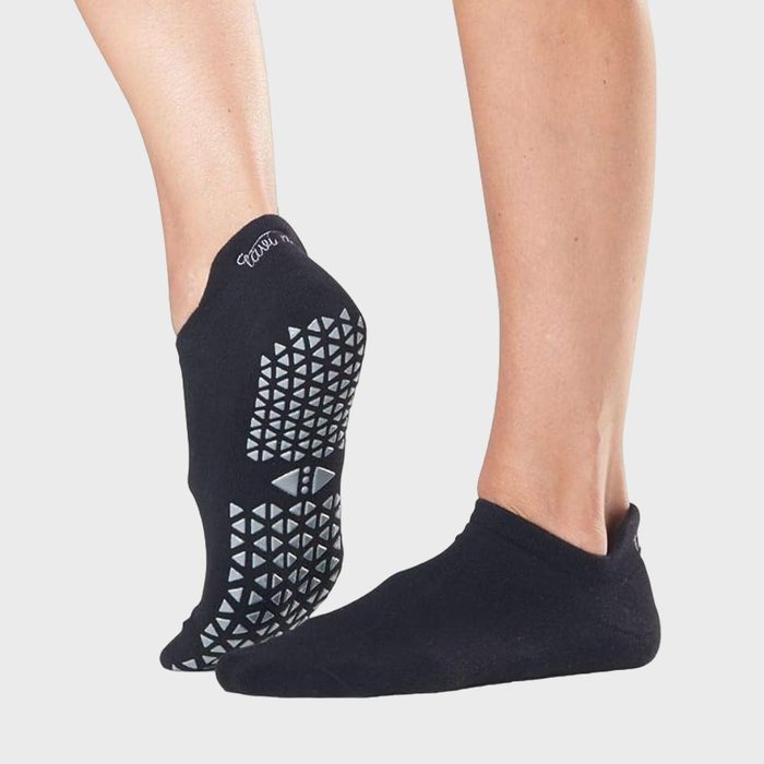 Black socks with rubber grip patterns, worn by two feet, against a light gray background.