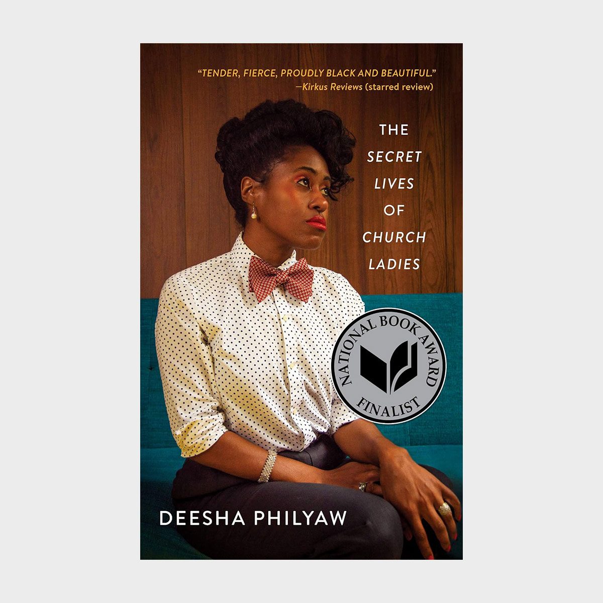 Woman sits wearing a polka-dot shirt and bow tie, against a wooden panel backdrop. Text: "The Secret Lives of Church Ladies" by Deesha Philyaw.