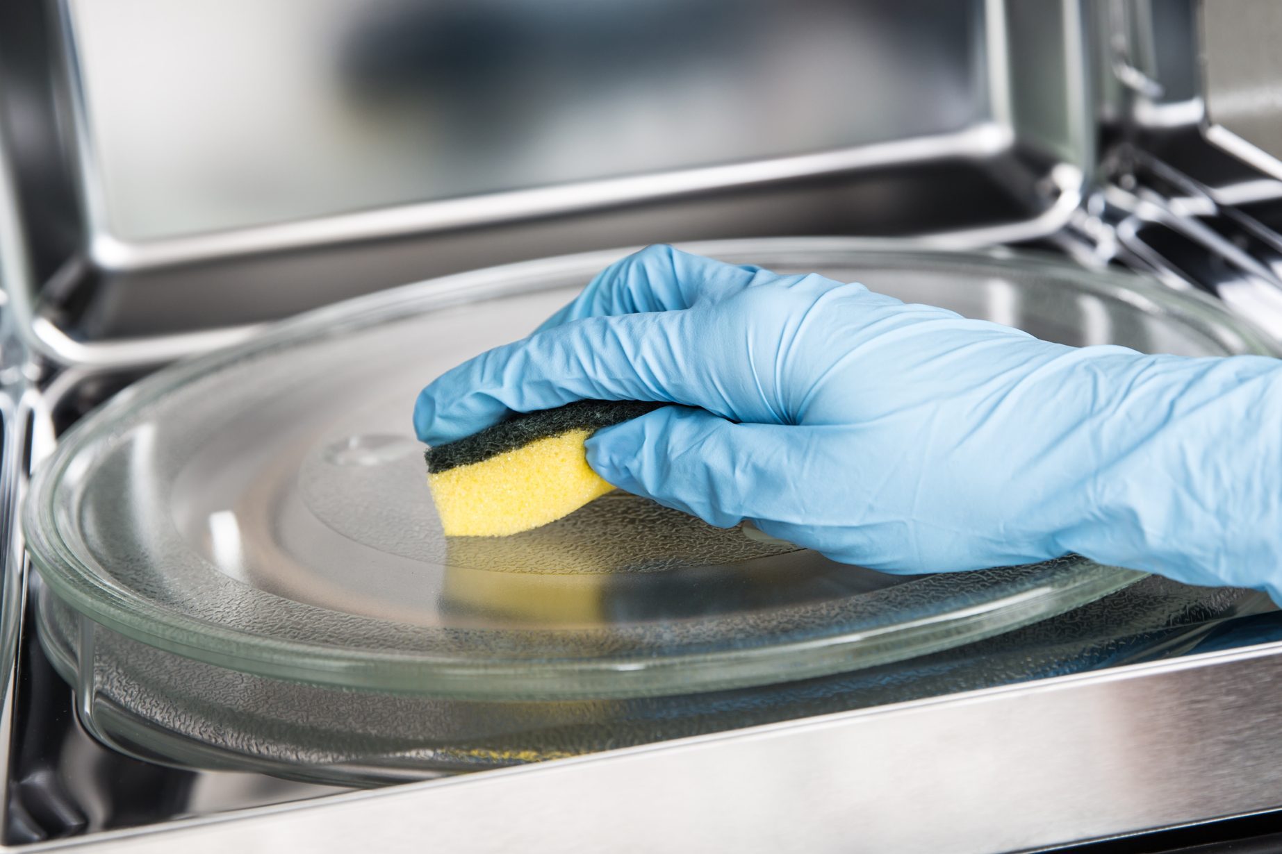 Woman hand cleaning microwave oven with sponge