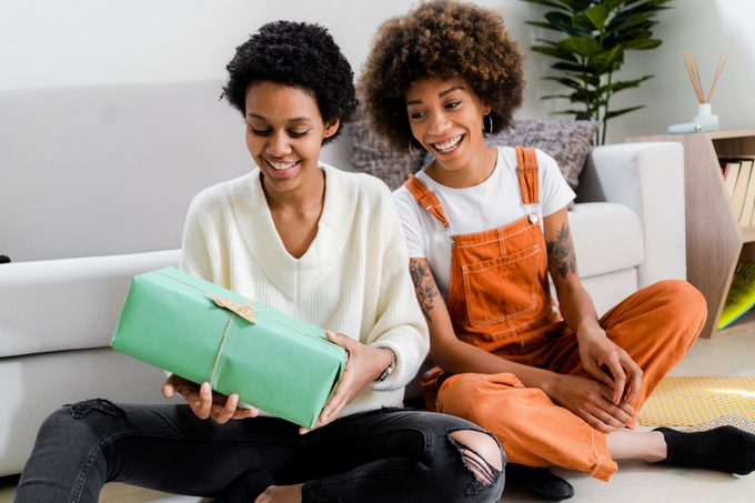 Portrait of two friends sitting on the floor at home looking at gift