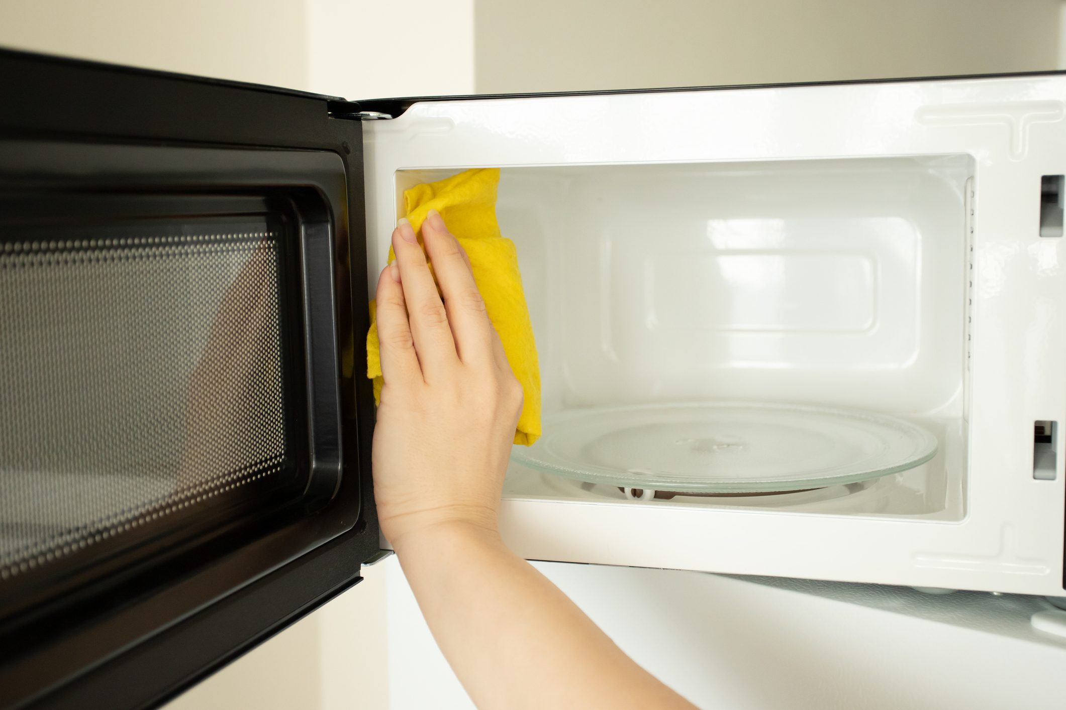 a woman's hand washes a microwave with a rag, cleanliness and hygiene in the kitchen