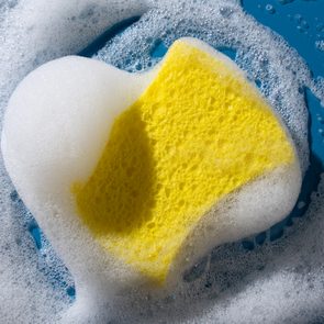 Yellow sponge surrounded by foamy white bubbles, resting on a blue wet surface.