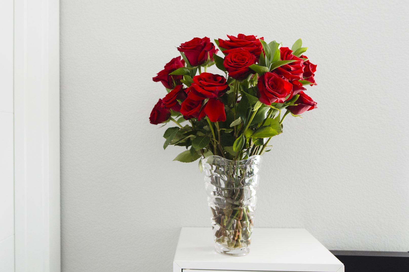 Close-up of roses in vase on table by wall at home