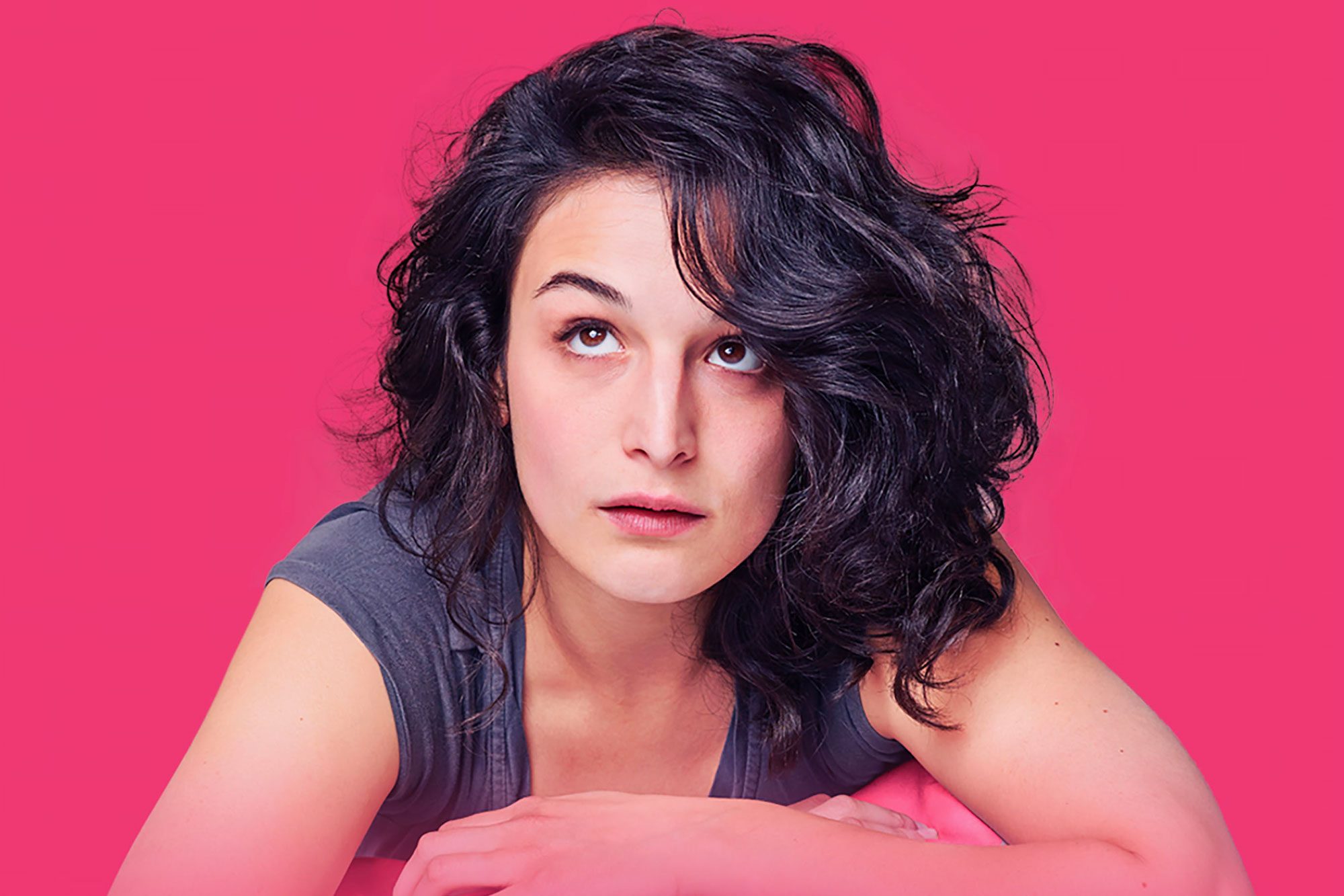Person gazes upward, resting on forearms, against a solid pink background.