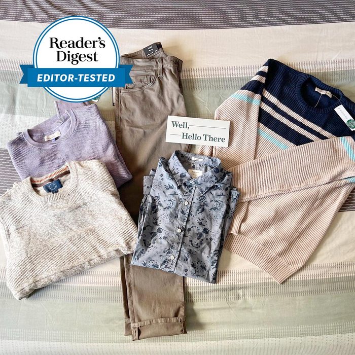 Clothing items displayed on a bed include sweaters, pants, and a floral shirt. A 