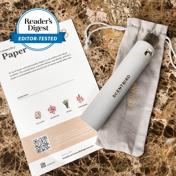 Perfume bottle rests on a drawstring pouch beside a product card; marble table surface. 