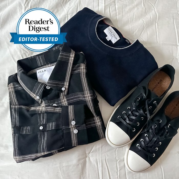 Plaid shirt, folded; navy sweater beside it; black sneakers with white toe caps, all on a white fabric background. 
