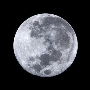 The full moon shines brightly against a dark, starless night sky, revealing detailed lunar craters and surface patterns.