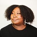 Person looking slightly to the side wears a black shirt and hoop earrings, set against a plain white background.